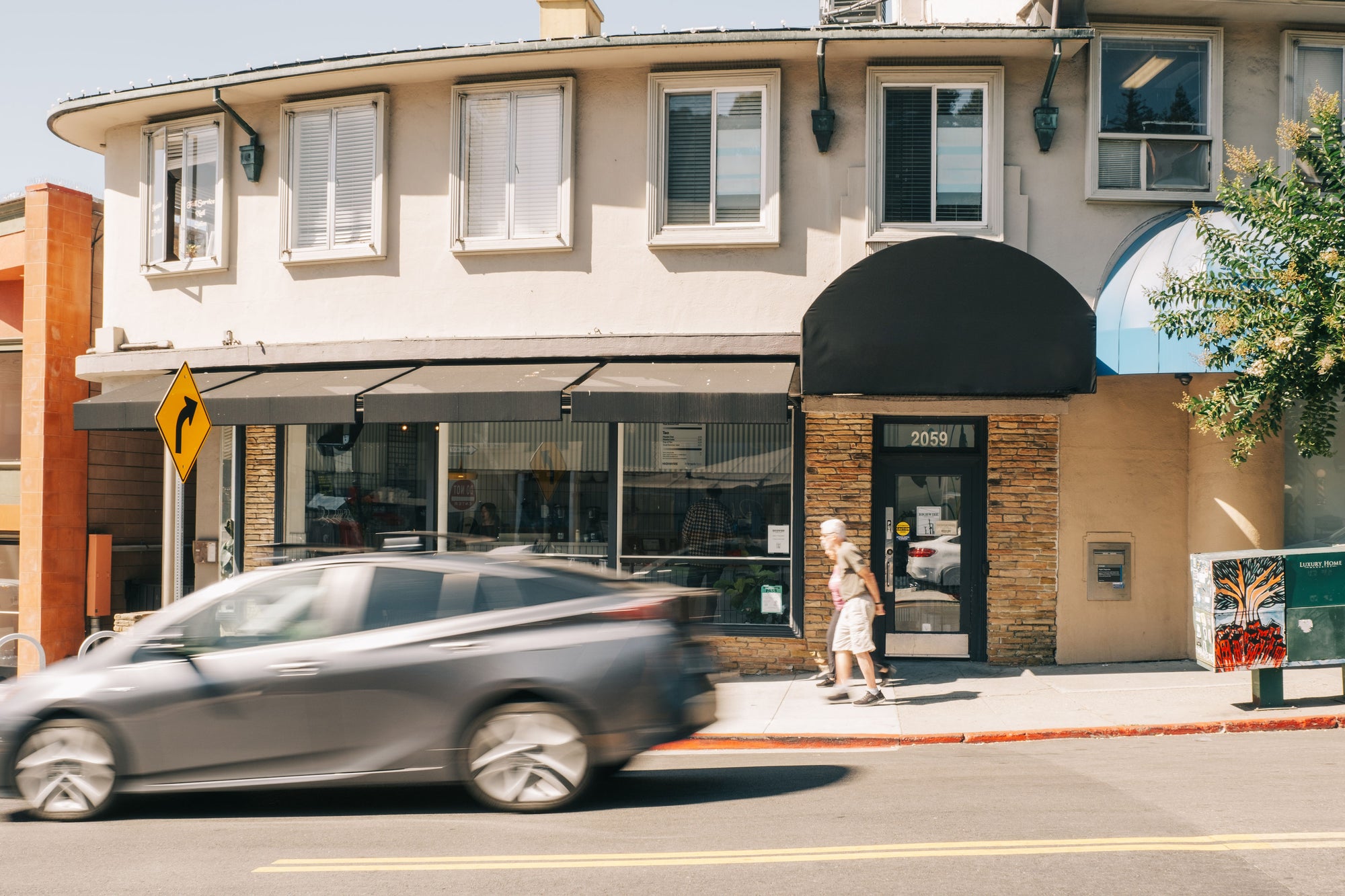 The curved storefront of Highwire's coffee shop in Montclair. A car and pedestrians passing by.