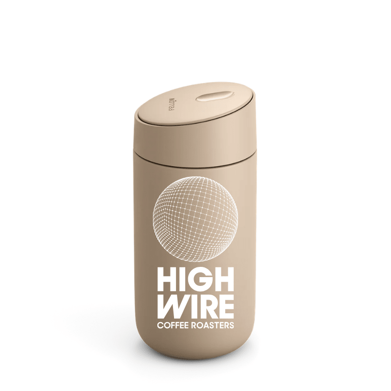 Light brown thermal mug with slide lid, with a geometric graphic and Highwire Coffee Roasters printed in white.