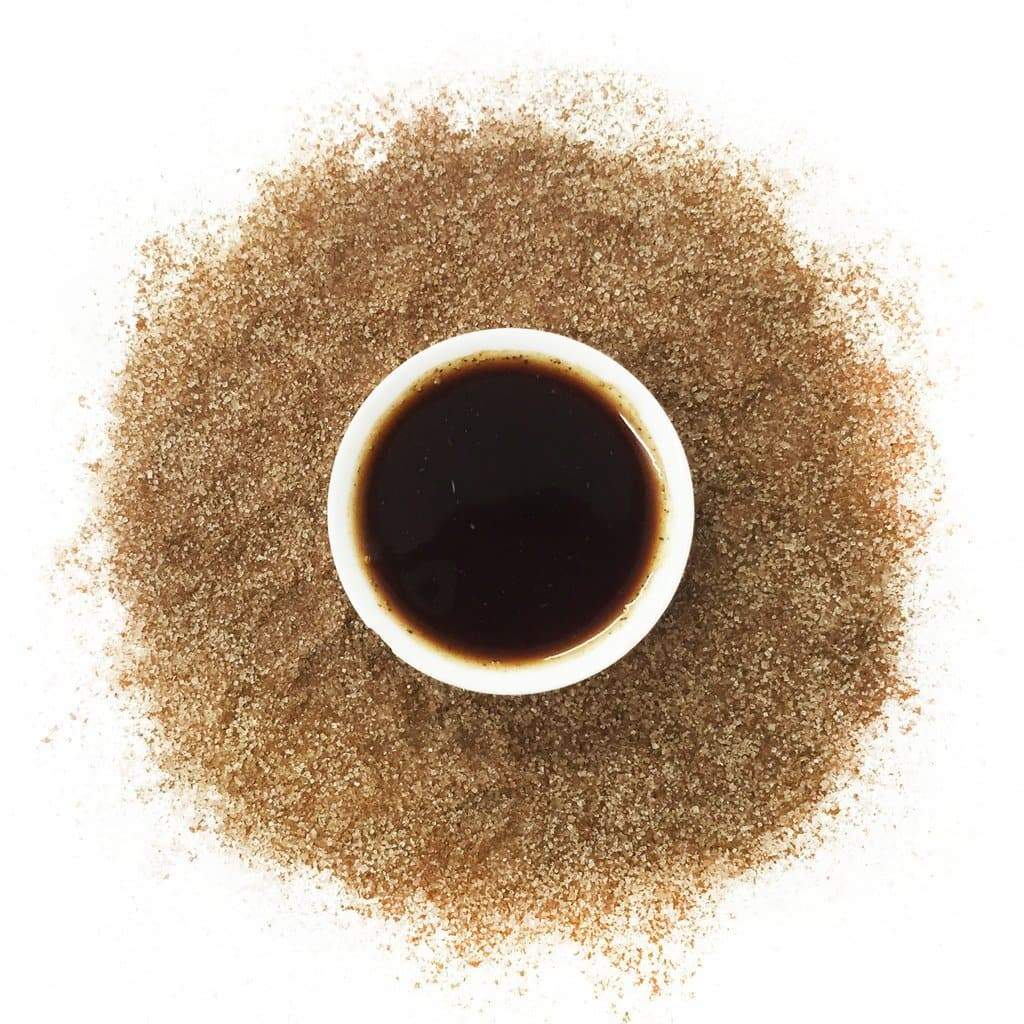 Top-down view of a cup of spiced tea surrounded by finely ground tea and spices on a white background