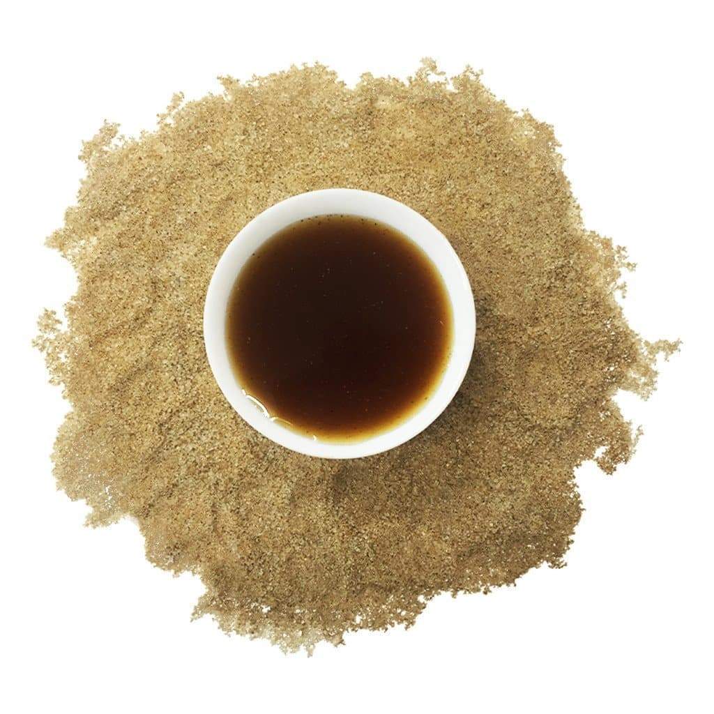 Cup of brewed tea with micro-ground spices surrounding it on a white background
